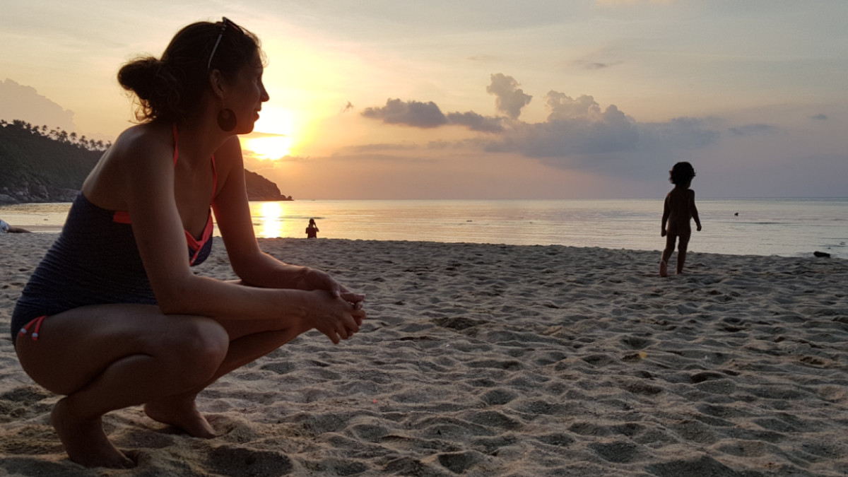 woman kneeling at the beach looking towards her son, the sun goes down in the back